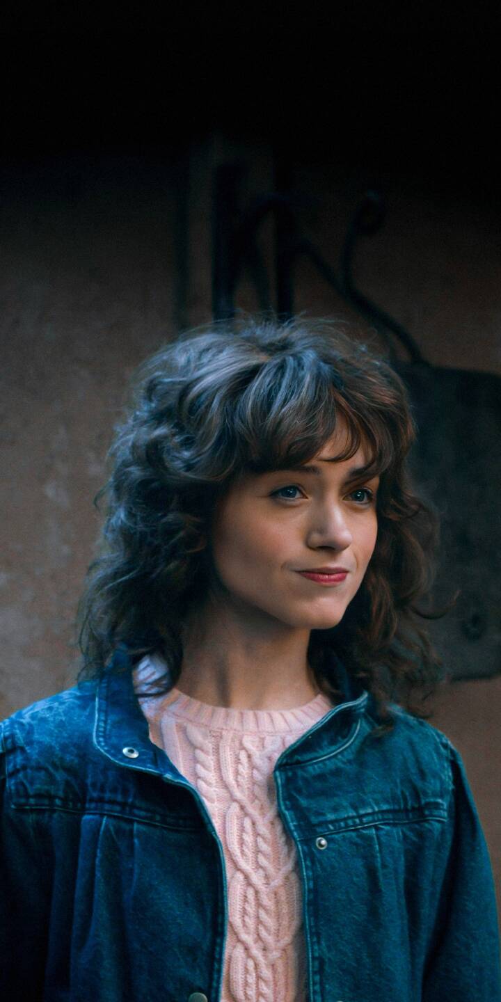 This iPhone wallpaper features Natalia Dyer in stunning 4K detail. She wears a blue jean jacket over a pink cable-knit sweater, set against a rustic, textured background, making this wallpaper a visually compelling choice. | netflix portrait actor iphone hd stranger things series scifi mobile celebrity android nancy wheeler 4k wallpaper hd wallpaper actress blue jacket 4KWallpaper TVShow StrangerThings natalia dyer pink sweater NancyWheeler NataliaDyer MoodyLighting DenimJacket PinkSweater PensiveGaze background pensive This iPhone wallpaper features Natalia Dyer in stunning 4K detail. She wears a blue jean jacket over a pink cable-knit sweater, set against a rustic, textured background, making this wallpaper a visually compelling choice.