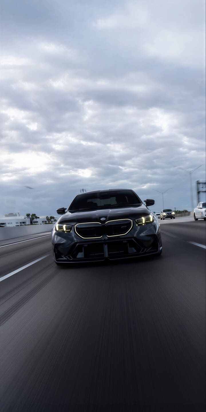 Elevate your iPhone with this stunning 4K BMW M5 wallpaper, featuring the powerful black car driving on a highway under a cloudy sky, illuminated by its iconic yellow headlights. This dynamic automotive wallpaper perfectly captures the sleek design and speed of the BMW M5 for a captivating mobile display. | car sports car highway iphone bmw m5 black car bmw m5 mobile 4k wallpaper hd wallpaper automotive Elevate your iPhone with this stunning 4K BMW M5 wallpaper, featuring the powerful black car driving on a highway under a cloudy sky, illuminated by its iconic yellow headlights. This dynamic automotive wallpaper perfectly captures the sleek design and speed of the BMW M5 for a captivating mobile display.