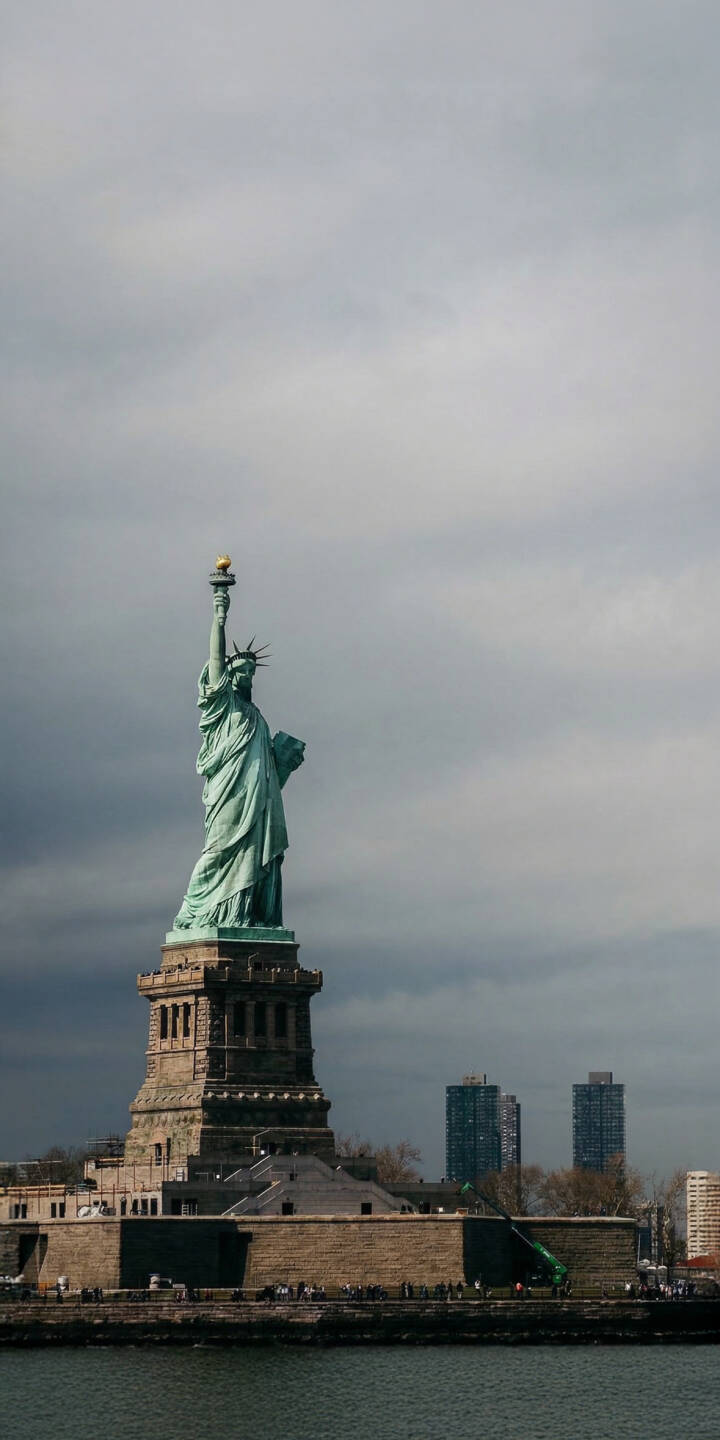 Elevate your iPhone screen with this stunning 4K Statue of Liberty wallpaper, showcasing Lady Liberty's iconic greenish patina against a dramatic, cloudy sky with water in the foreground. This high-quality wallpaper is perfect for anyone seeking a powerful symbol of freedom for their device. | landmark new york usa iphone cloudy sky mobile nyc 4k wallpaper hd wallpaper monument statue of liberty lady liberty Elevate your iPhone screen with this stunning 4K Statue of Liberty wallpaper, showcasing Lady Liberty's iconic greenish patina against a dramatic, cloudy sky with water in the foreground. This high-quality wallpaper is perfect for anyone seeking a powerful symbol of freedom for their device.