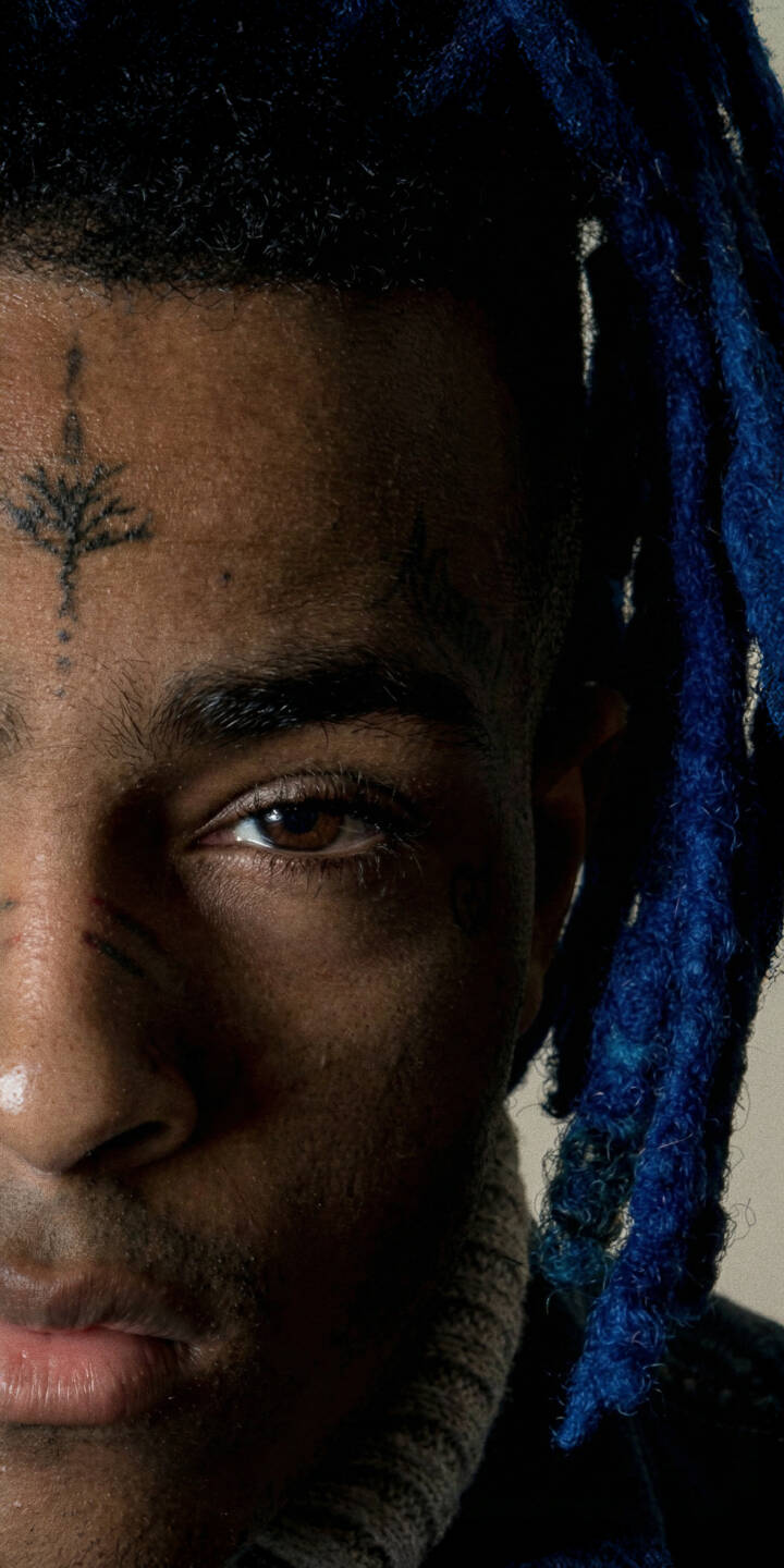 The intense gaze of XXXTentacion's brown eye pierces through dramatic shadows, highlighted by his vibrant blue dreadlocks and distinctive facial tattoos in this striking 4K wallpaper – an essential iPhone wallpaper for fans. | rapper portrait xxxtentacion iphone wallpaper hip hop mobile 4k wallpaper hd wallpaper dark aesthetic jahseh onfroy blue dreads The intense gaze of XXXTentacion's brown eye pierces through dramatic shadows, highlighted by his vibrant blue dreadlocks and distinctive facial tattoos in this striking 4K wallpaper – an essential iPhone wallpaper for fans.
