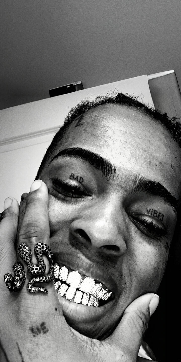 XXXTENTACION's striking diamond grillz sparkle prominently, sharply contrasting with the distinct "BAD" and "VIBES" eyelid tattoos visible in this raw, monochrome 4K wallpaper. This powerful visual is an essential wallpaper for iPhone users looking to represent the artist's unique legacy. | rapper xxxtentacion iphone wallpaper hip hop grillz mobile 4k wallpaper hd wallpaper monochrome tattoos jahseh onfroy XXXTENTACION's striking diamond grillz sparkle prominently, sharply contrasting with the distinct "BAD" and "VIBES" eyelid tattoos visible in this raw, monochrome 4K wallpaper. This powerful visual is an essential wallpaper for iPhone users looking to represent the artist's unique legacy.