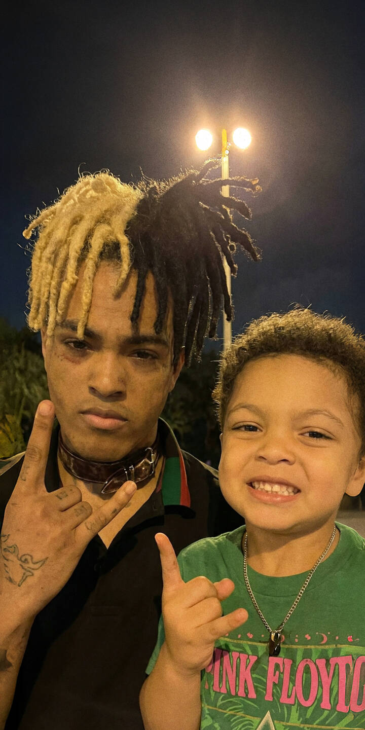 XXXTentacion's distinctive two-tone dreadlocks and spiked collar stand out alongside a smiling child, both making a 'rock-on' gesture in this unique 4K wallpaper. This powerful moment makes an excellent iPhone wallpaper for fans. | rapper xxxtentacion iphone wallpaper hip hop mobile 4k wallpaper hd wallpaper rock on dreads jahseh onfroy two-tone hair XXXTentacion's distinctive two-tone dreadlocks and spiked collar stand out alongside a smiling child, both making a 'rock-on' gesture in this unique 4K wallpaper. This powerful moment makes an excellent iPhone wallpaper for fans.