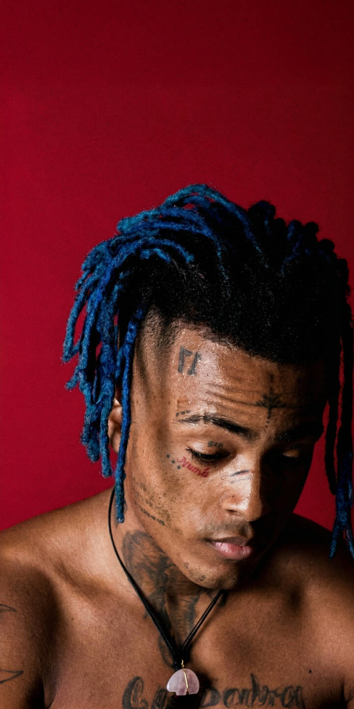 XXXTENTACION's signature blue dreadlocks pop against the bold red backdrop in this evocative 4K wallpaper, perfectly capturing his pensive gaze and distinctive face tattoos. This must-have XXXTENTACION wallpaper is ideal for customizing your iPhone screen. | aesthetic rapper music xxxtentacion iphone wallpaper mobile 4k wallpaper hd wallpaper red background jahseh onfroy blue dreads XXXTENTACION's signature blue dreadlocks pop against the bold red backdrop in this evocative 4K wallpaper, perfectly capturing his pensive gaze and distinctive face tattoos. This must-have XXXTENTACION wallpaper is ideal for customizing your iPhone screen.