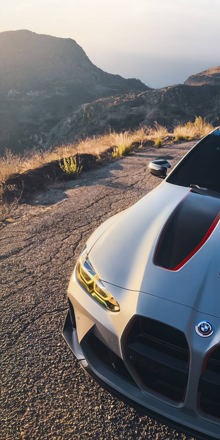 Sunlight gleams across the sleek grey hood of the BMW M4, its yellow headlights piercing the dawn light on a winding mountain road in this striking 4K wallpaper. This stunning automotive wallpaper is perfect for personalizing your iPhone with a blend of luxury and natural beauty. | sports car mountain iphone bmw wallpaper bmw m4 mobile luxury car golden hour 4k wallpaper hd wallpaper automotive Sunlight gleams across the sleek grey hood of the BMW M4, its yellow headlights piercing the dawn light on a winding mountain road in this striking 4K wallpaper. This stunning automotive wallpaper is perfect for personalizing your iPhone with a blend of luxury and natural beauty.