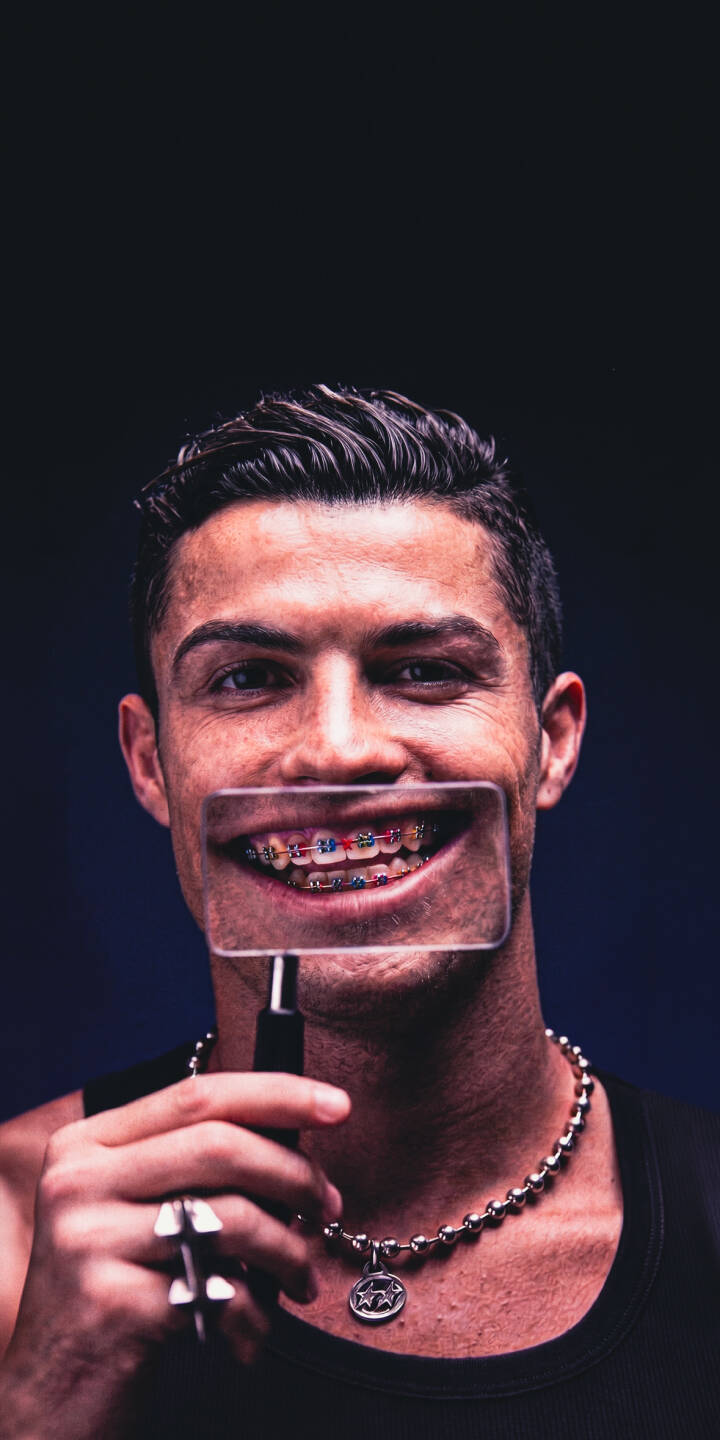Cristiano Ronaldo's vibrant, colorful braces are dramatically magnified through a lens in this striking 4K wallpaper, making it a truly unique wallpaper for any iPhone. His confident smile and subtle necklace details enhance this personal, engaging shot. | portrait smile iphone ronaldo wallpaper cr7 cristiano ronaldo mobile 4k wallpaper hd wallpaper braces magnified Cristiano Ronaldo's vibrant, colorful braces are dramatically magnified through a lens in this striking 4K wallpaper, making it a truly unique wallpaper for any iPhone. His confident smile and subtle necklace details enhance this personal, engaging shot.