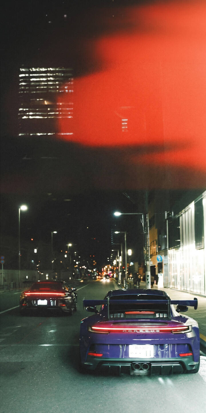 A vibrant purple Porsche GT3 leads on a city street, its taillights glowing bright red under a dramatic, cinematic red light leak, making for an eye-catching 4K wallpaper. This dynamic street scene is a must-have wallpaper for iPhone users who appreciate high-performance cars. | sports car city iphone porsche gt3 wallpaper night drive mobile red light 4k wallpaper hd wallpaper automotive A vibrant purple Porsche GT3 leads on a city street, its taillights glowing bright red under a dramatic, cinematic red light leak, making for an eye-catching 4K wallpaper. This dynamic street scene is a must-have wallpaper for iPhone users who appreciate high-performance cars.