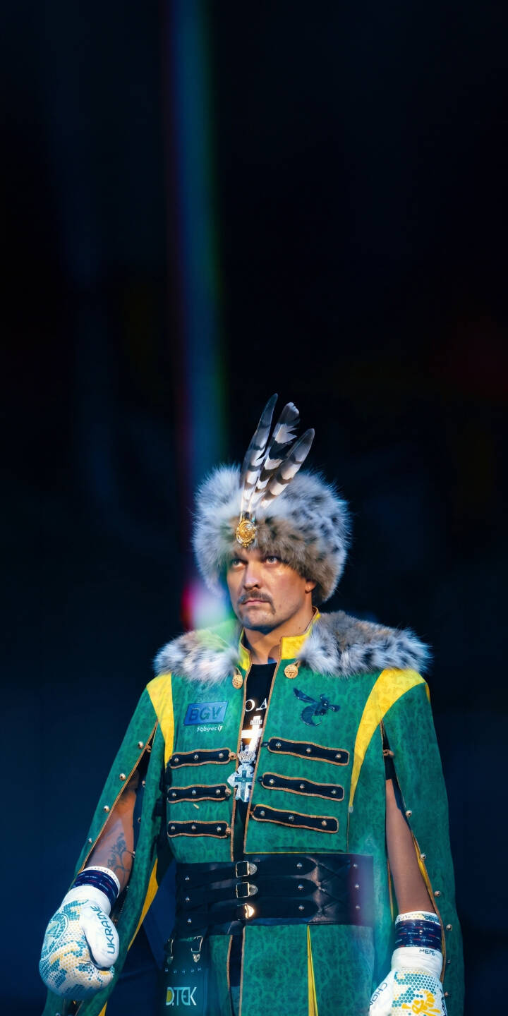 The vibrant green and yellow of Oleksandr Usyk's traditional Ukrainian coat stands out, topped with a distinctive fur hat and feathers, in this dramatic 4K wallpaper. This powerful boxer's entrance is a compelling wallpaper for any iPhone, capturing a unique cultural moment. | sports boxer boxing iphone wallpaper mobile 4k wallpaper hd wallpaper oleksandr usyk usyk ukrainian cossack The vibrant green and yellow of Oleksandr Usyk's traditional Ukrainian coat stands out, topped with a distinctive fur hat and feathers, in this dramatic 4K wallpaper. This powerful boxer's entrance is a compelling wallpaper for any iPhone, capturing a unique cultural moment.