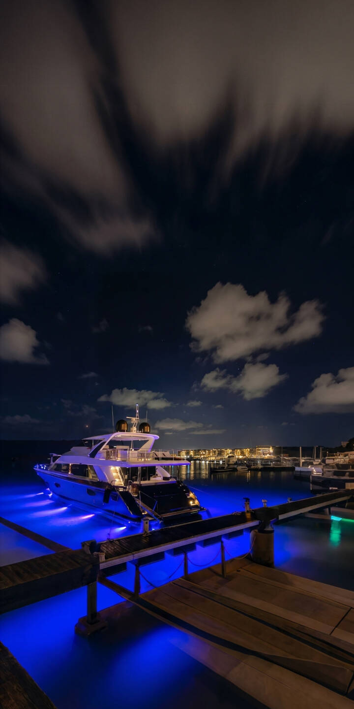Vibrant blue underwater lights cast an ethereal glow around a sleek white luxury yacht, creating a stunning 4K wallpaper perfect for iPhone users. This serene night marina scene is an exquisite wallpaper, showcasing blurred clouds above and distant city lights. | aesthetic night yacht iphone ocean wallpaper mobile 4k wallpaper hd wallpaper blue lights luxury yacht marina Vibrant blue underwater lights cast an ethereal glow around a sleek white luxury yacht, creating a stunning 4K wallpaper perfect for iPhone users. This serene night marina scene is an exquisite wallpaper, showcasing blurred clouds above and distant city lights.