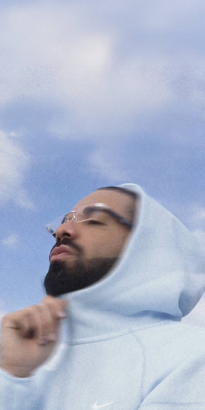 Drake's eyes are closed and his face upturned towards a bright, cloudy sky, creating a serene mood in this stunning 4K wallpaper. Dressed in a light blue Nike hoodie and sporting his signature glasses, this is an essential Drake wallpaper for iPhone. | aesthetic rapper sky iphone drake wallpaper mobile celebrity 4k wallpaper hd wallpaper ovo blue hoodie Drake's eyes are closed and his face upturned towards a bright, cloudy sky, creating a serene mood in this stunning 4K wallpaper. Dressed in a light blue Nike hoodie and sporting his signature glasses, this is an essential Drake wallpaper for iPhone.
