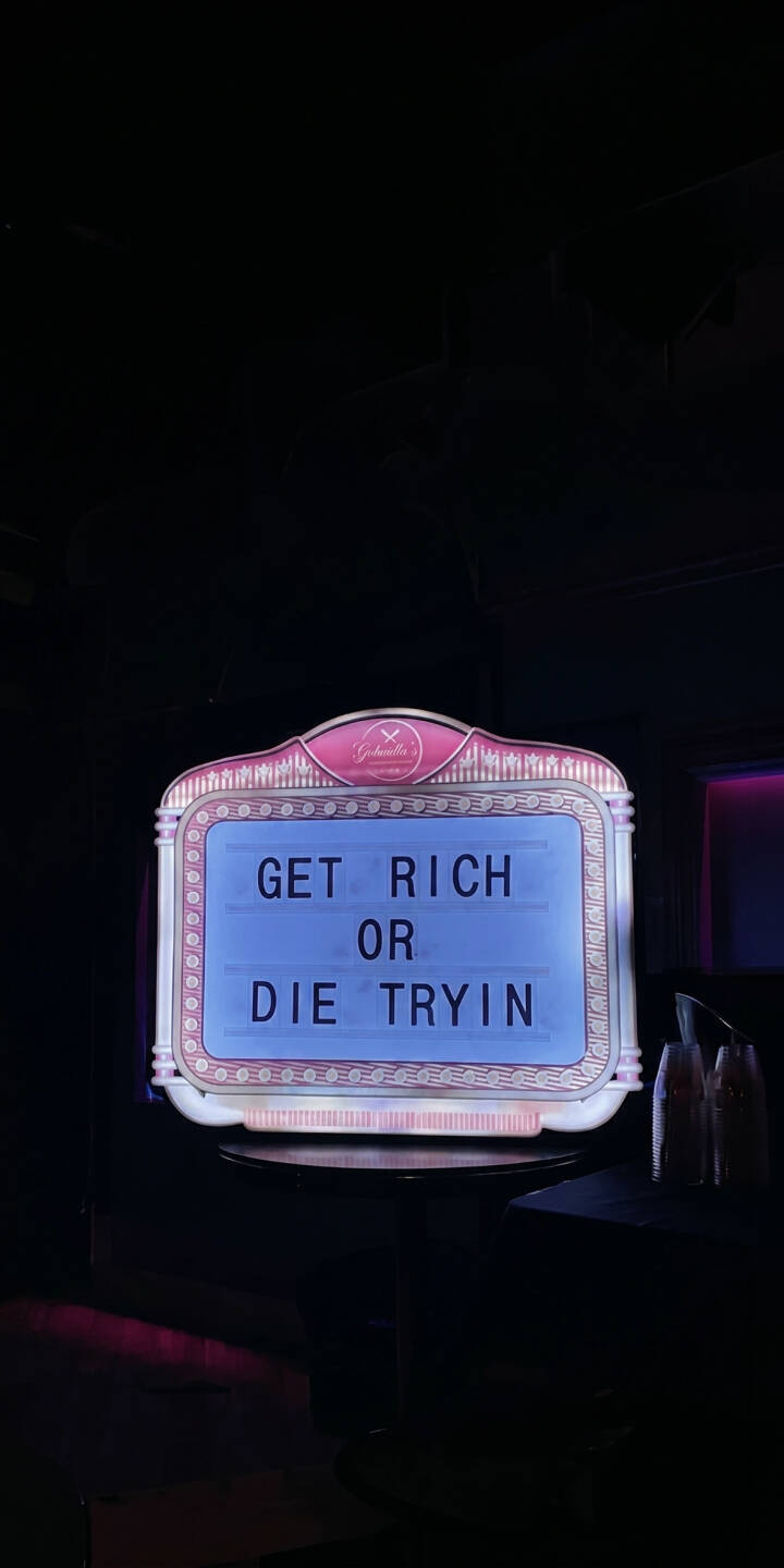 The bold blue text of 'GET RICH OR DIE TRYIN' glows intensely from a retro, pink-bordered light-up sign in this moody 4K wallpaper, making it an inspiring wallpaper for any iPhone user. This striking piece captures the vibrant neon illumination against a dark background, perfect for adding a motivational touch to your device. | aesthetic sign quote neon motivational iphone retro wallpaper mobile 4k wallpaper hd wallpaper get rich or die tryin The bold blue text of 'GET RICH OR DIE TRYIN' glows intensely from a retro, pink-bordered light-up sign in this moody 4K wallpaper, making it an inspiring wallpaper for any iPhone user. This striking piece captures the vibrant neon illumination against a dark background, perfect for adding a motivational touch to your device.