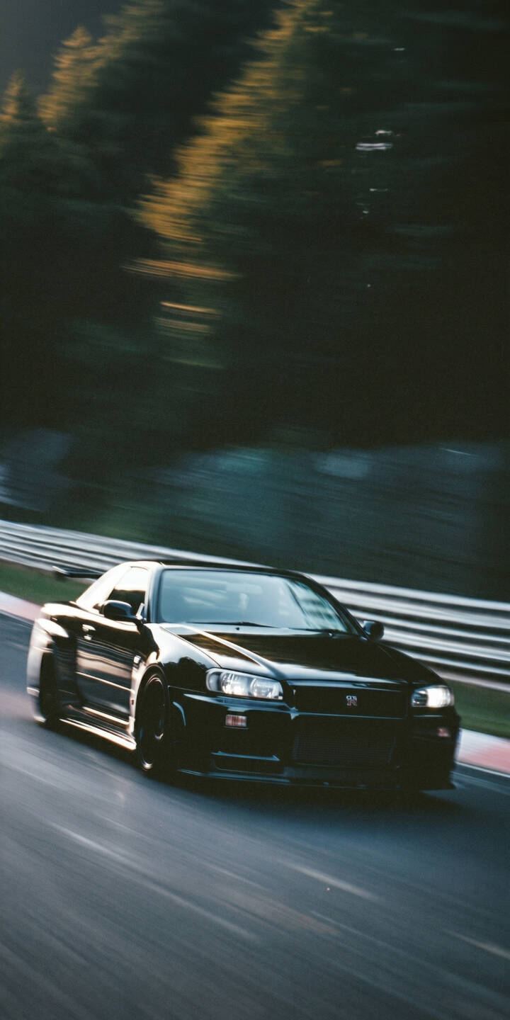 The iconic black Nissan Skyline R34 GT-R streaks across the track with dynamic motion blur, its headlights glowing brightly against the dark forest background in this thrilling 4K wallpaper. This high-speed racing wallpaper is perfect for personalizing your iPhone. | sports car dark iphone wallpaper racing nissan skyline mobile 4k wallpaper hd wallpaper gt-r r34 gtr motion blur The iconic black Nissan Skyline R34 GT-R streaks across the track with dynamic motion blur, its headlights glowing brightly against the dark forest background in this thrilling 4K wallpaper. This high-speed racing wallpaper is perfect for personalizing your iPhone.