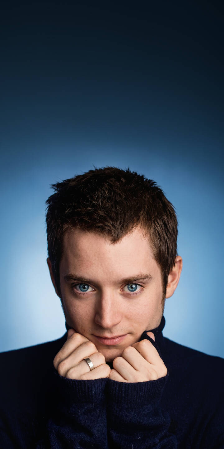 Elijah Wood's piercing blue eyes captivate the viewer as he gently holds the dark turtleneck collar in this striking 4K wallpaper. A must-have wallpaper for iPhone, it also highlights a subtle silver ring on his finger against a simple gradient blue background. | portrait actor iphone wallpaper blue eyes mobile celebrity 4k wallpaper hd wallpaper turtleneck elijah wood frodo baggins Elijah Wood's piercing blue eyes captivate the viewer as he gently holds the dark turtleneck collar in this striking 4K wallpaper. A must-have wallpaper for iPhone, it also highlights a subtle silver ring on his finger against a simple gradient blue background.