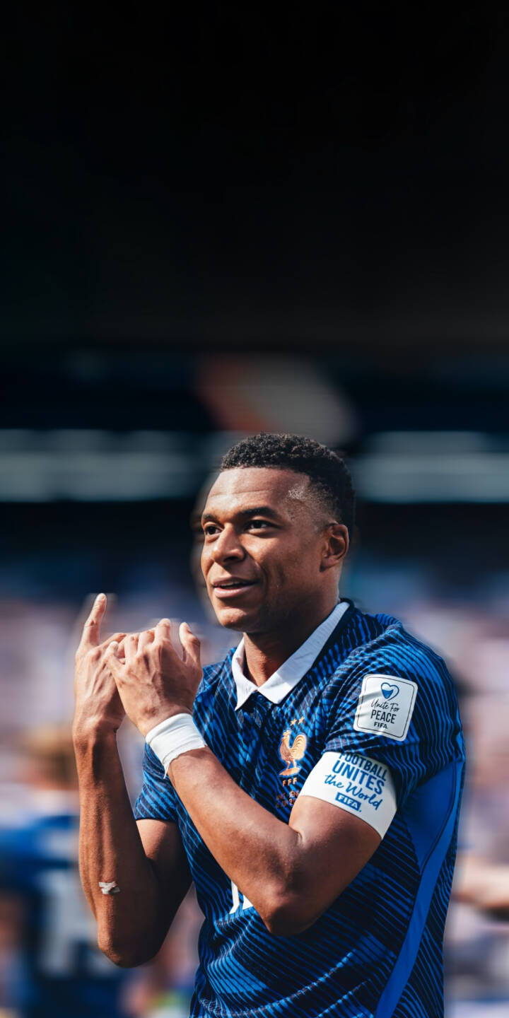 Kylian Mbappe flashes a bright smile while making a celebratory gesture, donning his blue French national team jersey and 'FOOTBALL UNITES THE WORLD' armband in this striking 4K wallpaper. This dynamic wallpaper is a perfect fit for any iPhone, capturing the iconic footballer's spirit. | football athlete celebration iphone france mbappe soccer wallpaper mobile 4k wallpaper hd wallpaper kylian mbappe Kylian Mbappe flashes a bright smile while making a celebratory gesture, donning his blue French national team jersey and 'FOOTBALL UNITES THE WORLD' armband in this striking 4K wallpaper. This dynamic wallpaper is a perfect fit for any iPhone, capturing the iconic footballer's spirit.