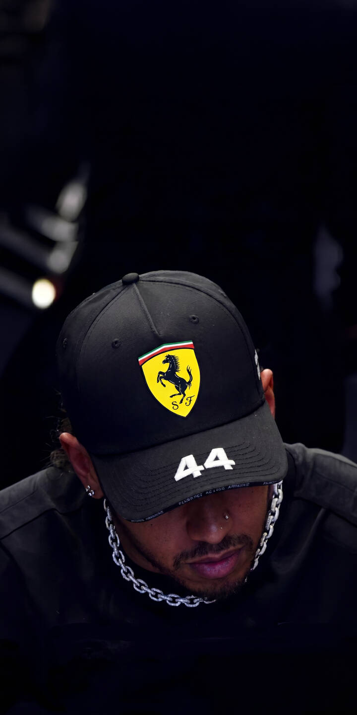 The bright yellow Scuderia Ferrari logo stands out prominently on Lewis Hamilton's black cap as he looks contemplatively downward in this striking 4K wallpaper. This pensive portrait, complete with his silver chain necklace, makes for an aesthetic wallpaper perfectly optimized for iPhone. | portrait iphone ferrari wallpaper f1 lewis hamilton formula 1 mobile 4k wallpaper hd wallpaper scuderia ferrari pensive The bright yellow Scuderia Ferrari logo stands out prominently on Lewis Hamilton's black cap as he looks contemplatively downward in this striking 4K wallpaper. This pensive portrait, complete with his silver chain necklace, makes for an aesthetic wallpaper perfectly optimized for iPhone.
