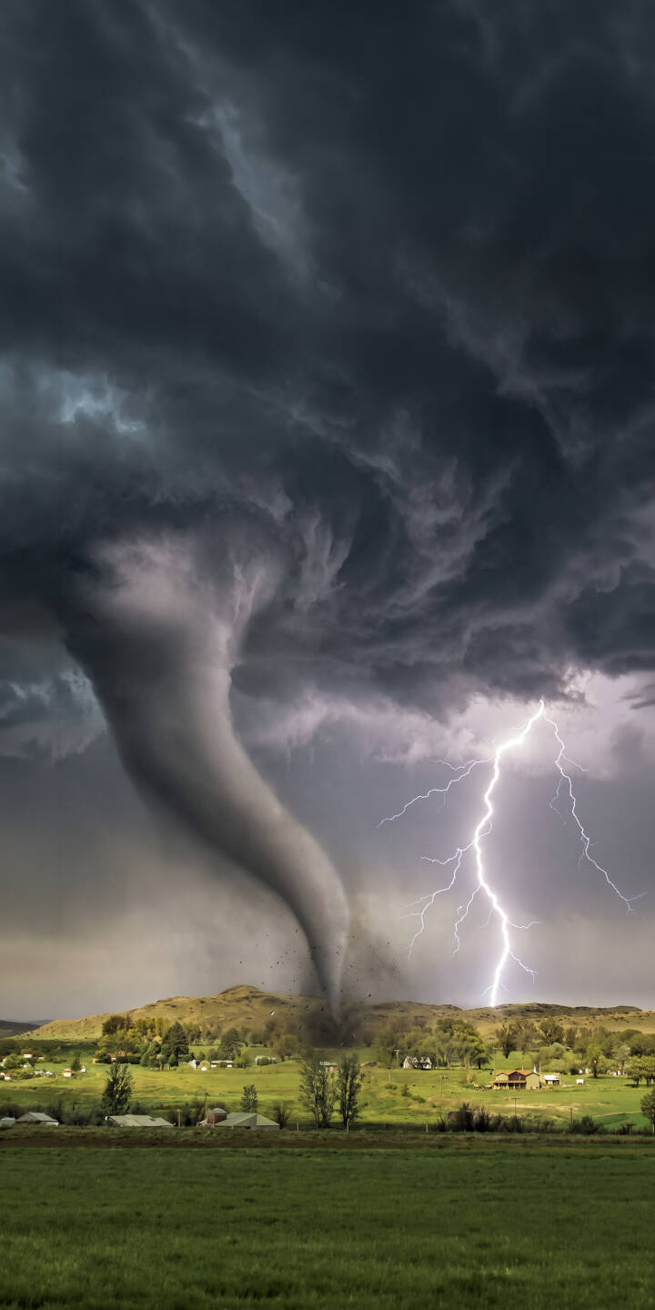 A colossal twisting funnel cloud dominates the landscape, with a bright jagged lightning bolt dramatically illuminating the ominous dark storm clouds in this breathtaking 4K wallpaper. This powerful nature wallpaper, perfect for iPhone, captures the destructive beauty of a severe storm.