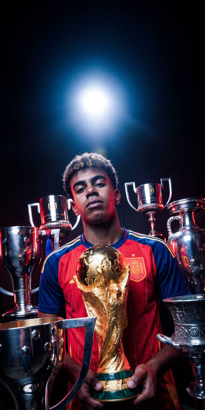 Bathed in a dramatic spotlight, a young footballer in a Spain jersey proudly clutches the gleaming golden FIFA World Cup trophy, surrounded by an array of silver awards in this striking 4K wallpaper. This triumphant moment makes a powerful statement on any iPhone with this stunning wallpaper. | football iphone soccer spain wallpaper champion mobile 4k wallpaper hd wallpaper world cup dramatic fifa trophy Bathed in a dramatic spotlight, a young footballer in a Spain jersey proudly clutches the gleaming golden FIFA World Cup trophy, surrounded by an array of silver awards in this striking 4K wallpaper. This triumphant moment makes a powerful statement on any iPhone with this stunning wallpaper.