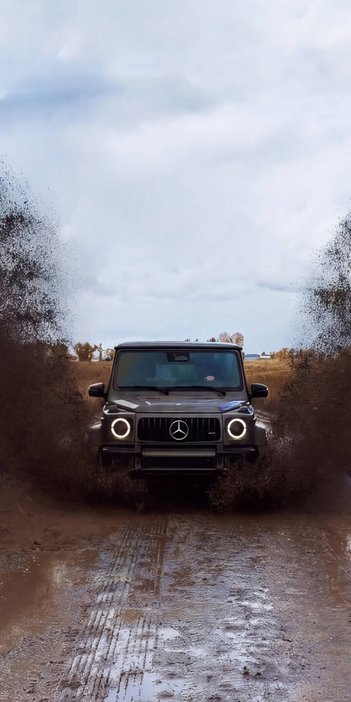 Muddy water explodes outwards as a powerful Mercedes G-Wagen (G-Class) charges through, its round headlights brightly illuminated, creating an epic 4K wallpaper perfect for iPhone. This thrilling off-road scene makes an exhilarating mobile wallpaper. | iphone mercedes wallpaper mobile 4k wallpaper hd wallpaper g wagon splash g class luxury suv offroad mud Muddy water explodes outwards as a powerful Mercedes G-Wagen (G-Class) charges through, its round headlights brightly illuminated, creating an epic 4K wallpaper perfect for iPhone. This thrilling off-road scene makes an exhilarating mobile wallpaper.