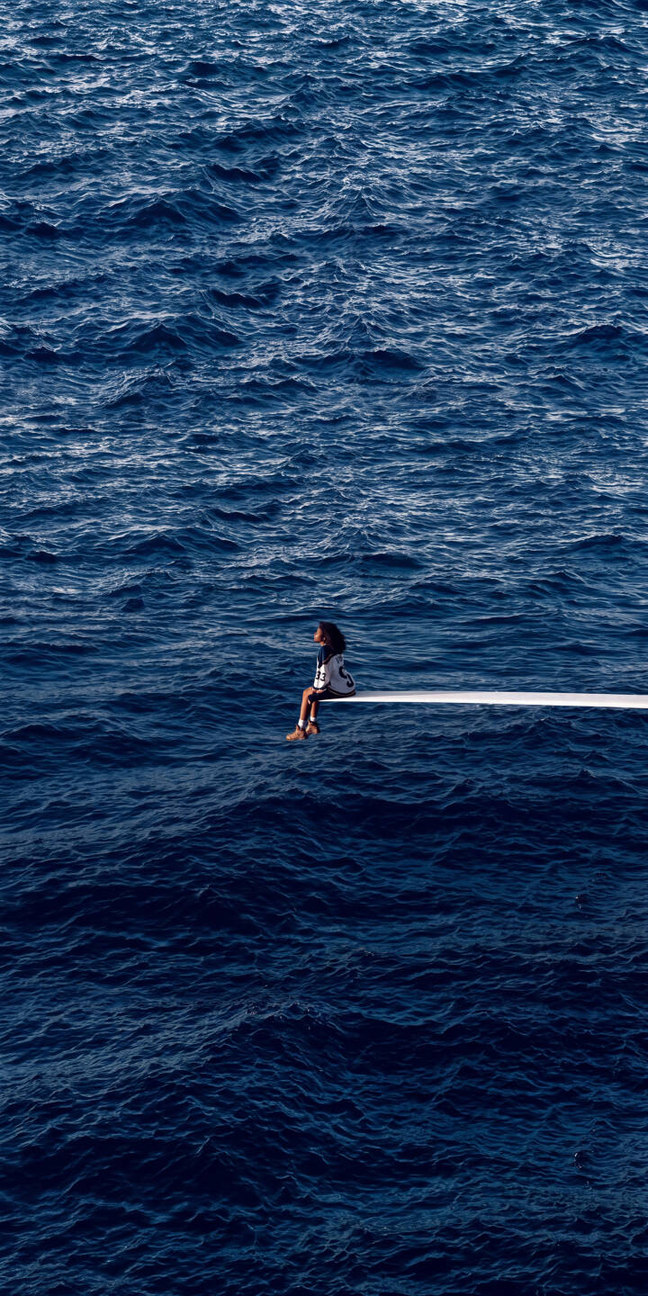 A lone figure, embodying SZA's iconic SOS album cover, sits contemplatively on a stark white platform extending into the vast, deep blue ocean in this stunning 4K wallpaper. This atmospheric wallpaper is perfect for iPhone users seeking a serene and aesthetic backdrop. | aesthetic blue iphone sza ocean minimalist wallpaper mobile solitude 4k wallpaper hd wallpaper sos album A lone figure, embodying SZA's iconic SOS album cover, sits contemplatively on a stark white platform extending into the vast, deep blue ocean in this stunning 4K wallpaper. This atmospheric wallpaper is perfect for iPhone users seeking a serene and aesthetic backdrop.