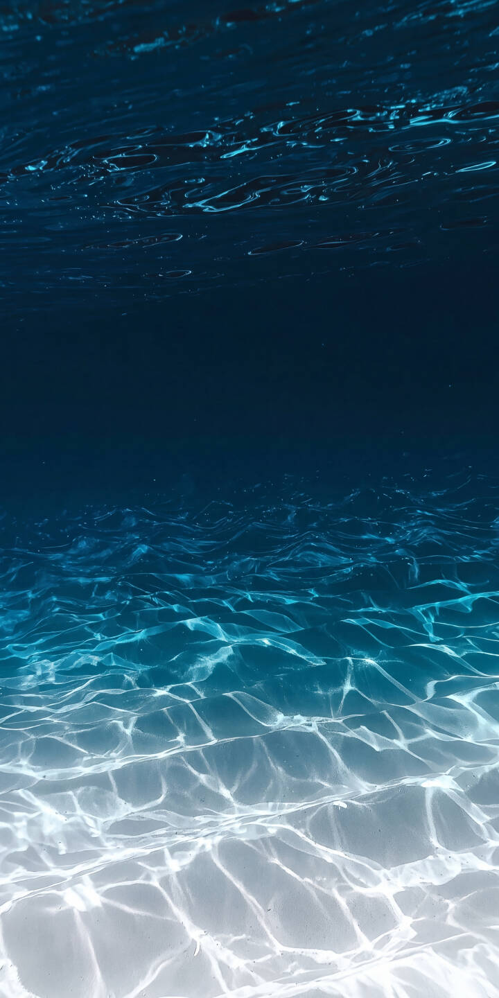 Ethereal light patterns shimmer across the water's surface, casting dancing reflections on the unseen bottom as the deep blue fades to a brilliant turquoise in this stunning 4K underwater wallpaper, a serene wallpaper for your iPhone. | blue underwater water light iphone ocean wallpaper mobile 4k wallpaper hd wallpaper ripples serene Ethereal light patterns shimmer across the water's surface, casting dancing reflections on the unseen bottom as the deep blue fades to a brilliant turquoise in this stunning 4K underwater wallpaper, a serene wallpaper for your iPhone.