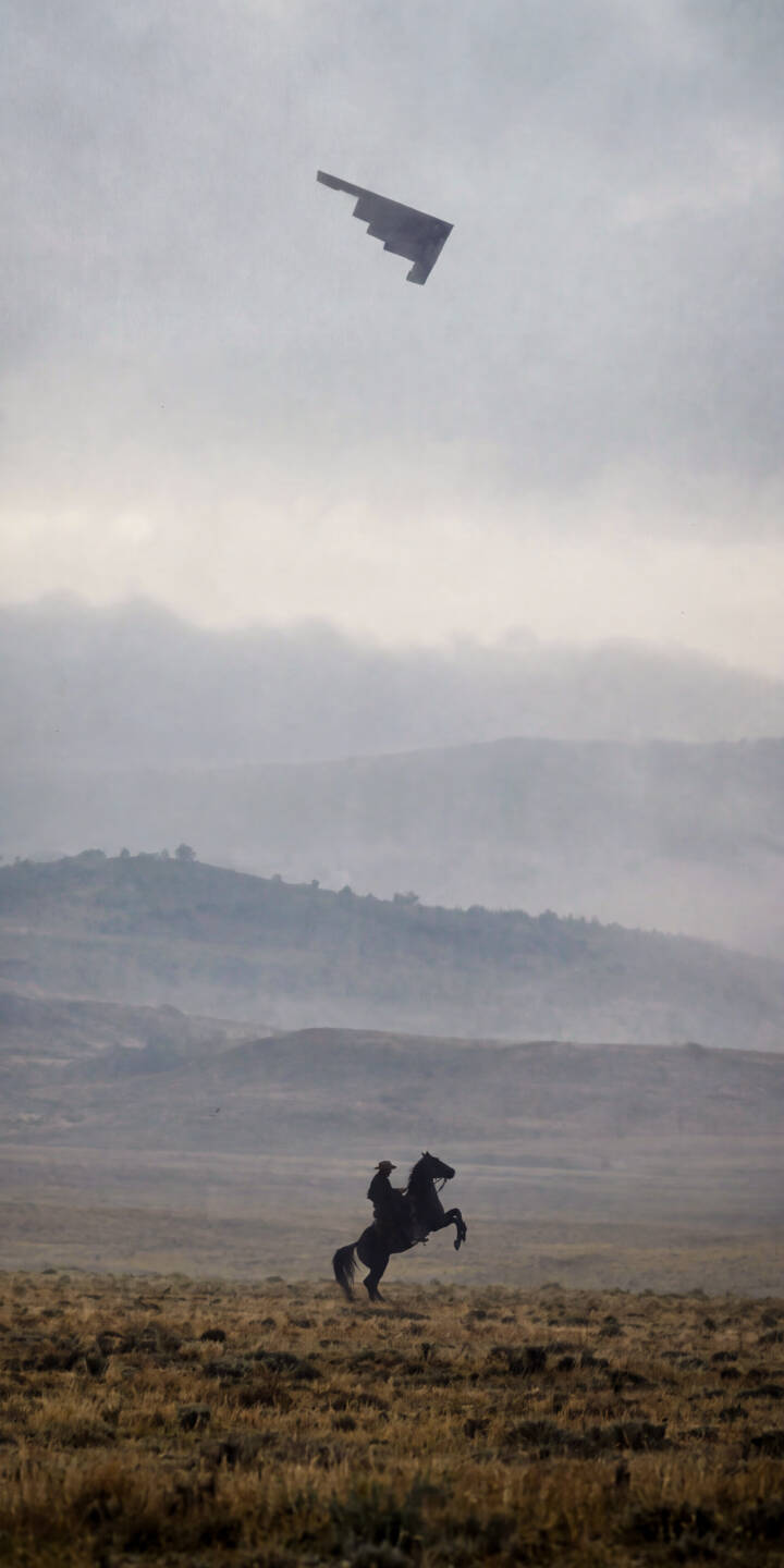 A powerful silhouette of a cowboy on a rearing horse dominates the misty grassland foreground, strikingly contrasted by the sleek B-2 Spirit bomber soaring through the overcast sky in this dramatic 4K wallpaper. This unique blend of classic Western and modern military themes makes for an essential iPhone wallpaper. | cowboy horse iphone wallpaper mobile 4k wallpaper hd wallpaper surreal western dramatic stealth bomber b-2 spirit A powerful silhouette of a cowboy on a rearing horse dominates the misty grassland foreground, strikingly contrasted by the sleek B-2 Spirit bomber soaring through the overcast sky in this dramatic 4K wallpaper. This unique blend of classic Western and modern military themes makes for an essential iPhone wallpaper.