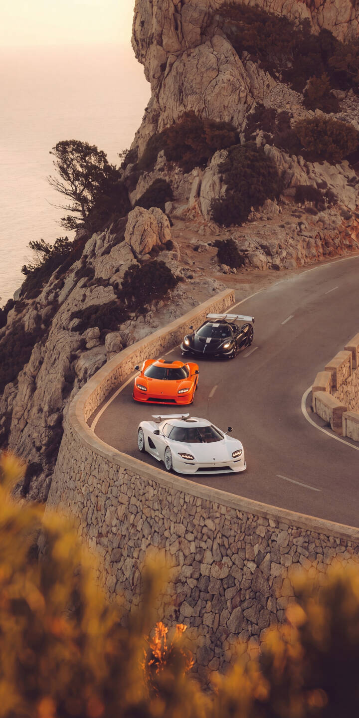 Three stunning Koenigsegg Jesko Attack hypercars, in white, orange, and black, carve through a breathtaking coastal road built into a rugged cliffside under the golden hour light in this exclusive 4K wallpaper. This dynamic scene makes for a superb car enthusiast's iPhone wallpaper. | sunset iphone luxury wallpaper hypercar koenigsegg mobile jesko 4k wallpaper hd wallpaper automotive coastal road Three stunning Koenigsegg Jesko Attack hypercars, in white, orange, and black, carve through a breathtaking coastal road built into a rugged cliffside under the golden hour light in this exclusive 4K wallpaper. This dynamic scene makes for a superb car enthusiast's iPhone wallpaper.