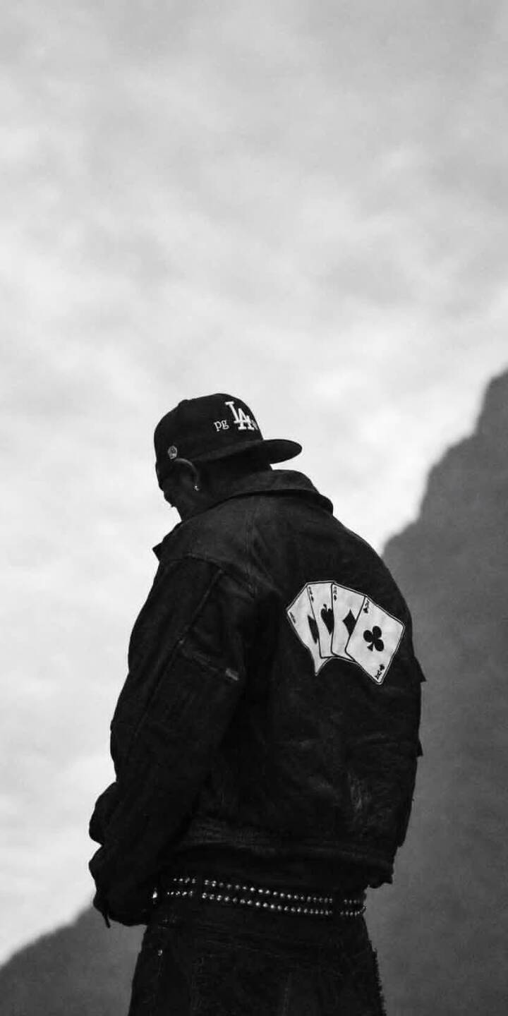 Three distinct playing cards, an Ace of Spades, Hearts, and Clubs, adorn the back of a figure's black denim jacket in this stylish monochrome 4K wallpaper for iPhone. This cool wallpaper also features a studded belt and an "LA" cap against a dramatic cloudy sky background. | artist Three distinct playing cards, an Ace of Spades, Hearts, and Clubs, adorn the back of a figure's black denim jacket in this stylish monochrome 4K wallpaper for iPhone. This cool wallpaper also features a studded belt and an "LA" cap against a dramatic cloudy sky background.