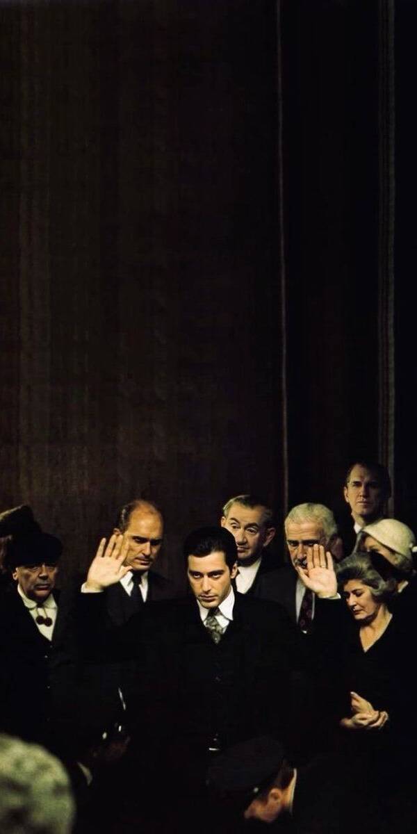 With a serious expression, Michael Corleone solemnly raises his right hand, taking an oath surrounded by a crowd in this iconic 4K movie wallpaper. This compelling visual is a perfect iPhone wallpaper for fans of The Godfather saga. | artist With a serious expression, Michael Corleone solemnly raises his right hand, taking an oath surrounded by a crowd in this iconic 4K movie wallpaper. This compelling visual is a perfect iPhone wallpaper for fans of The Godfather saga.