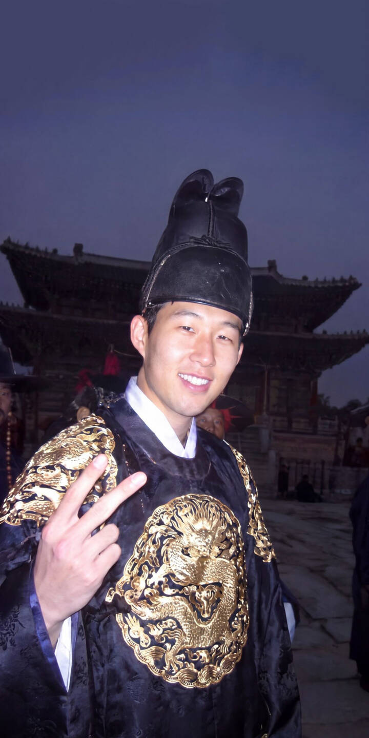 A cheerful smile and a peace sign greet the viewer in this vibrant 4K wallpaper, featuring a man in an ornate black traditional Korean royal robe with shimmering gold dragon embroidery, set against a classic palace backdrop — an ideal wallpaper for iPhone users seeking cultural elegance. | traditional dragon iphone wallpaper peace sign korean mobile culture 4k wallpaper hd wallpaper royal hanbok A cheerful smile and a peace sign greet the viewer in this vibrant 4K wallpaper, featuring a man in an ornate black traditional Korean royal robe with shimmering gold dragon embroidery, set against a classic palace backdrop — an ideal wallpaper for iPhone users seeking cultural elegance.