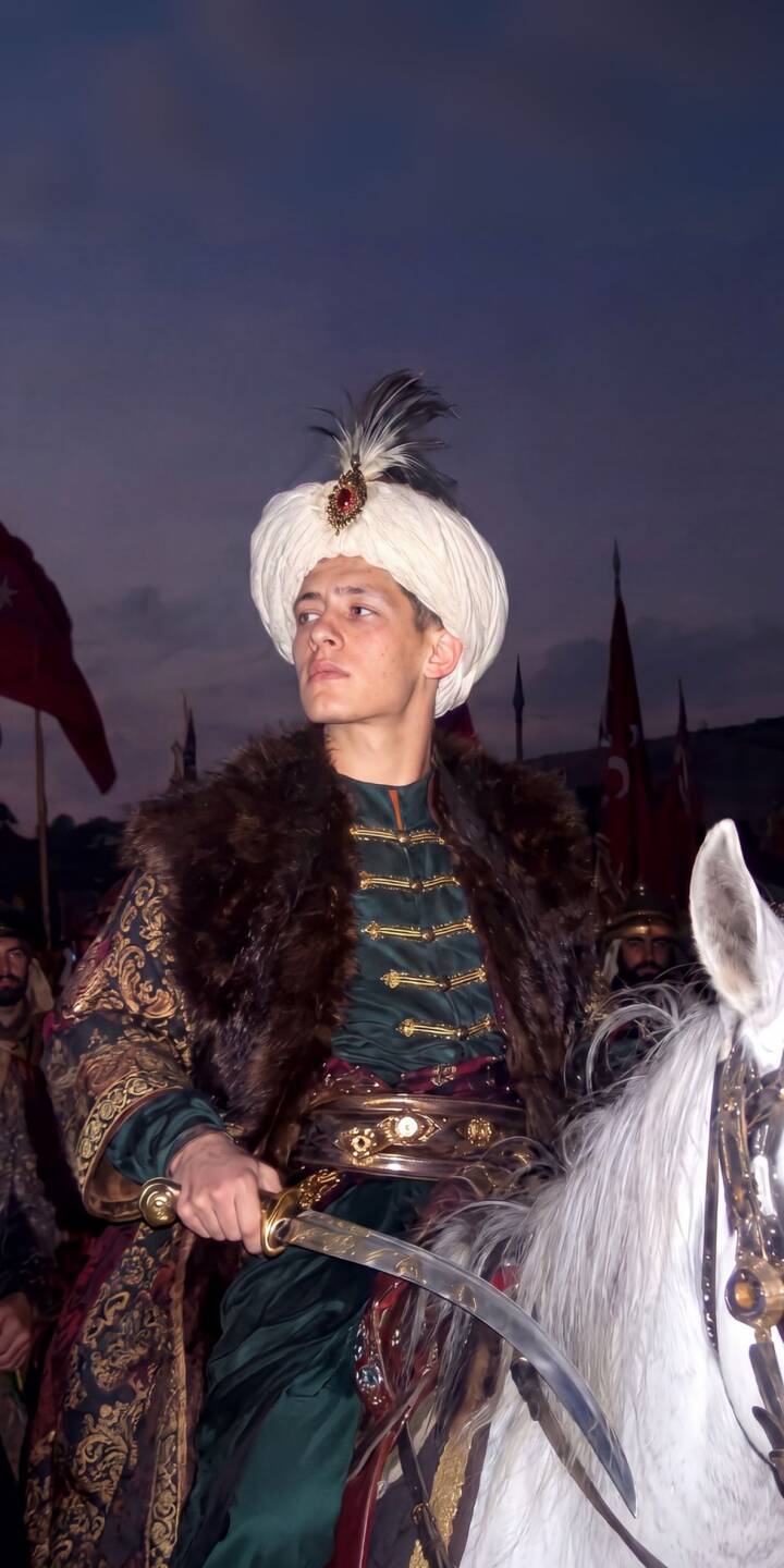 A determined young Ottoman Sultan, resplendent in his emerald tunic and fur-lined robe, wields a gleaming saber atop a white horse in this majestic 4K wallpaper. This stunning historical wallpaper is perfect for personalizing your iPhone screen. | warrior horse iphone sultan wallpaper mobile saber empire 4k wallpaper hd wallpaper historical ottoman A determined young Ottoman Sultan, resplendent in his emerald tunic and fur-lined robe, wields a gleaming saber atop a white horse in this majestic 4K wallpaper. This stunning historical wallpaper is perfect for personalizing your iPhone screen.