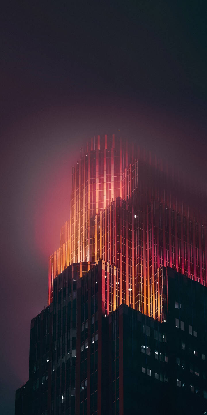 Vibrant red and orange light radiates from a sleek skyscraper, piercing through the surrounding mist in this dramatic 4K wallpaper – an atmospheric city wallpaper perfect for your iPhone. | city night foggy skyscraper iphone wallpaper mobile 4k wallpaper hd wallpaper red glow urban aesthetic Vibrant red and orange light radiates from a sleek skyscraper, piercing through the surrounding mist in this dramatic 4K wallpaper – an atmospheric city wallpaper perfect for your iPhone.