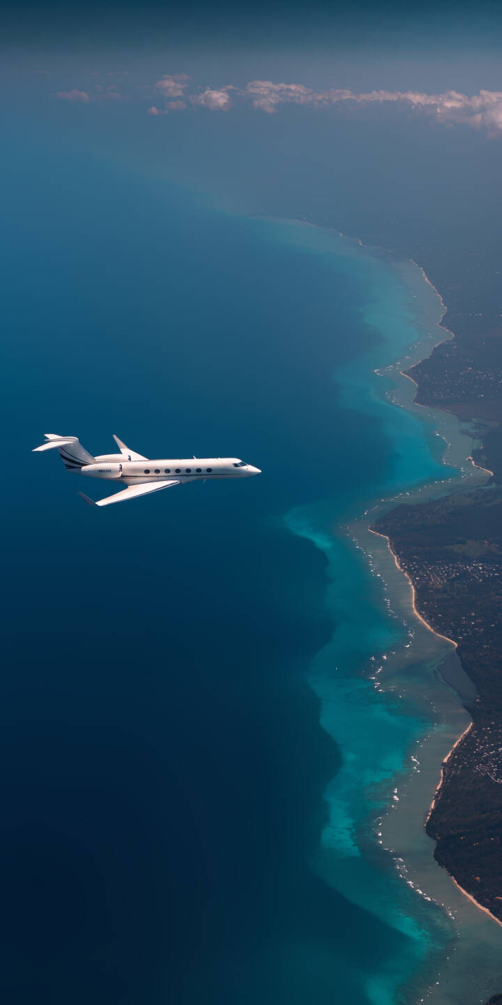 A sleek white private jet soars high above the stunning turquoise coastal waters and lush green land in this breathtaking 4K wallpaper, making an aspirational wallpaper for your iPhone. | travel coast iphone private jet ocean airplane wallpaper mobile aerial view blue aesthetic 4k wallpaper hd wallpaper A sleek white private jet soars high above the stunning turquoise coastal waters and lush green land in this breathtaking 4K wallpaper, making an aspirational wallpaper for your iPhone.
