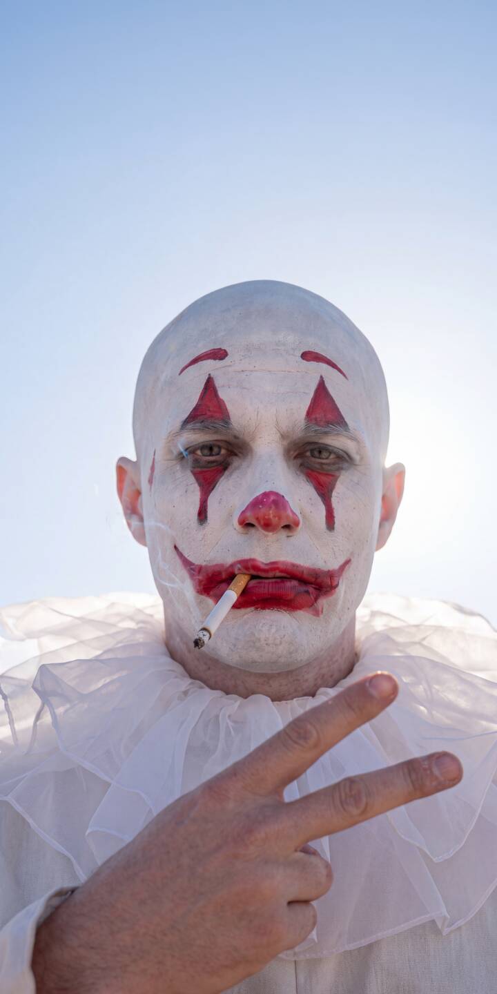 A cigarette dangles from the lips of an edgy, bald clown, featuring white face paint with dramatic red teardrops and a wide, painted smile, as he confidently flashes a peace sign against a vibrant blue sky in this compelling 4K wallpaper. This unique artwork is a must-have wallpaper for iPhone, offering a distinctive and modern aesthetic. | aesthetic portrait iphone wallpaper peace sign smoking clown mobile 4k wallpaper hd wallpaper edgy sad clown A cigarette dangles from the lips of an edgy, bald clown, featuring white face paint with dramatic red teardrops and a wide, painted smile, as he confidently flashes a peace sign against a vibrant blue sky in this compelling 4K wallpaper. This unique artwork is a must-have wallpaper for iPhone, offering a distinctive and modern aesthetic.