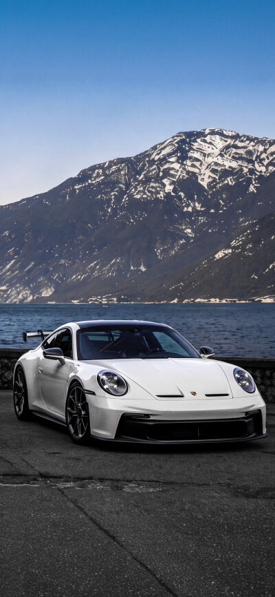 A vibrant blue Porsche 911 GT3 sports car is perfectly set against a stunning lake and rugged mountain landscape in this 4K iPhone wallpaper. This matching wallpaper, ideal for two screens, showcases the elegant car and picturesque scenery, making it a captivating mobile wallpaper.