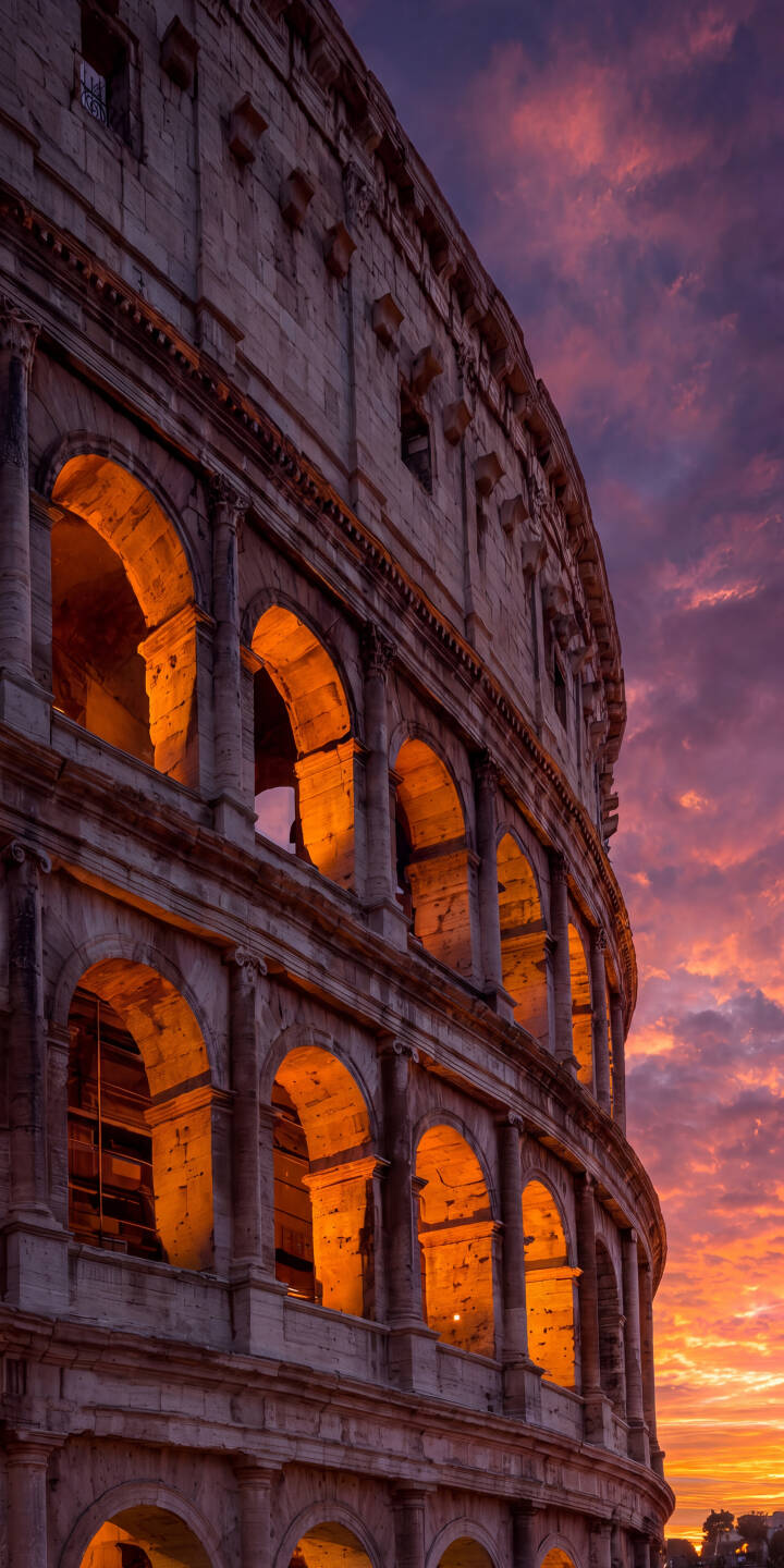 Dramatic purple and orange clouds paint a breathtaking backdrop to the ancient Colosseum as warm light glows from within its historic arches, making a stunning 4K wallpaper. This majestic Roman structure comes to life in a vibrant twilight display, offering an epic wallpaper for iPhone users. | sunset twilight architecture landmark iphone rome wallpaper mobile colosseum 4k wallpaper hd wallpaper ancient rome Dramatic purple and orange clouds paint a breathtaking backdrop to the ancient Colosseum as warm light glows from within its historic arches, making a stunning 4K wallpaper. This majestic Roman structure comes to life in a vibrant twilight display, offering an epic wallpaper for iPhone users.