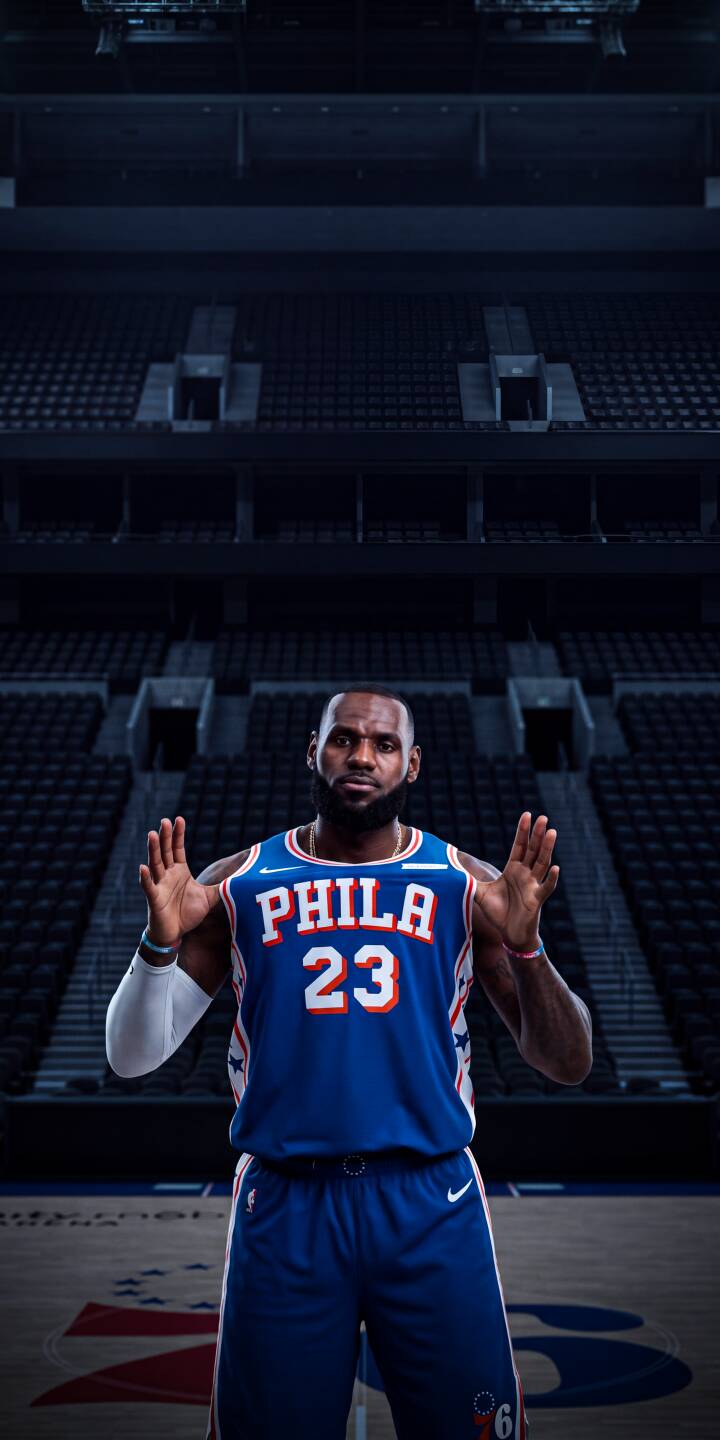 LeBron James stands with both hands raised in his vibrant blue Philadelphia 76ers number 23 jersey against a darkly lit, empty arena, creating a compelling 4K wallpaper perfect for iPhone. This intense moment provides a unique wallpaper for any basketball fan. | basketball nba sports lebron james lebron iphone wallpaper mobile 4k wallpaper hd wallpaper phila 76ers LeBron James stands with both hands raised in his vibrant blue Philadelphia 76ers number 23 jersey against a darkly lit, empty arena, creating a compelling 4K wallpaper perfect for iPhone. This intense moment provides a unique wallpaper for any basketball fan.