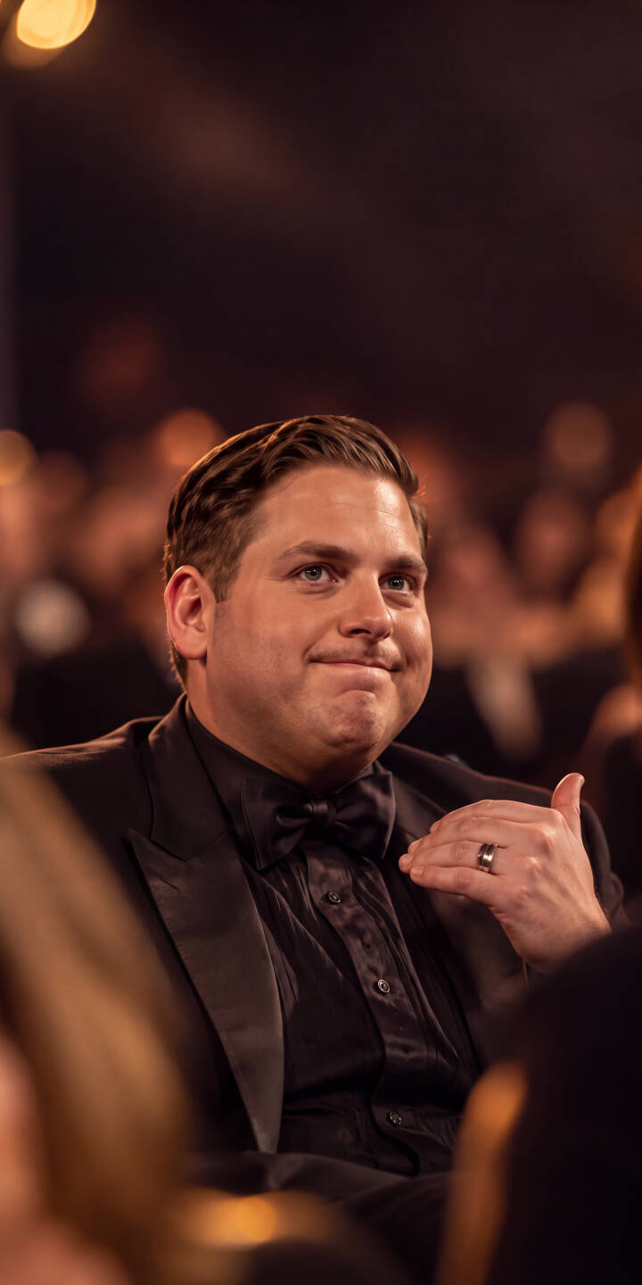 A subtle smirk plays on Jonah Hill's face as he sits sharply dressed in a black tuxedo, captured in the warm, blurred lights of an event in this stunning 4K wallpaper. This captivating moment makes for a sophisticated wallpaper for iPhone users looking for a celebrity touch. | portrait actor iphone wallpaper classy mobile celebrity event 4k wallpaper hd wallpaper tuxedo jonah hill A subtle smirk plays on Jonah Hill's face as he sits sharply dressed in a black tuxedo, captured in the warm, blurred lights of an event in this stunning 4K wallpaper. This captivating moment makes for a sophisticated wallpaper for iPhone users looking for a celebrity touch.
