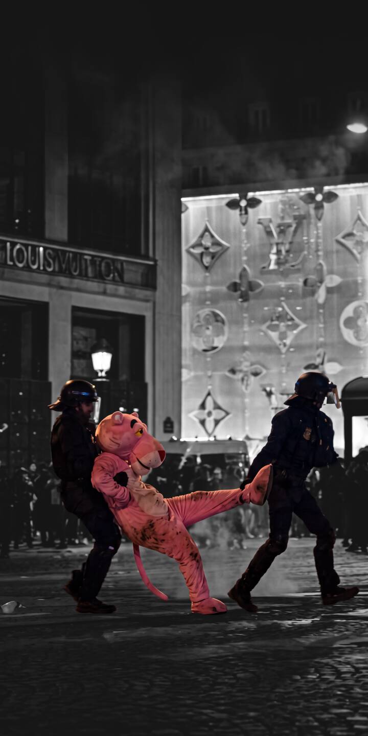 The iconic Pink Panther mascot in vibrant pink contrasts sharply with the monochromatic street scene, being escorted by figures in this striking 4K wallpaper for iPhone. This unique wallpaper features the famous character set against a blurry Louis Vuitton storefront at night. | urban street art iphone wallpaper louis vuitton pink panther mobile 4k wallpaper hd wallpaper mascot color splash The iconic Pink Panther mascot in vibrant pink contrasts sharply with the monochromatic street scene, being escorted by figures in this striking 4K wallpaper for iPhone. This unique wallpaper features the famous character set against a blurry Louis Vuitton storefront at night.