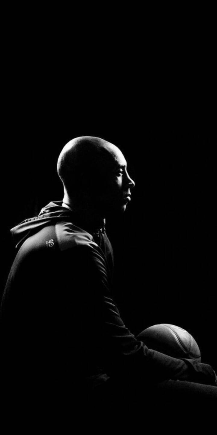 Deep shadows play across the legendary Kobe Bryant's profile as he intensely gazes into the distance, holding a basketball subtly in this evocative black and white 4K wallpaper — an essential wallpaper for iPhone showcasing the Mamba Mentality. | artist Deep shadows play across the legendary Kobe Bryant's profile as he intensely gazes into the distance, holding a basketball subtly in this evocative black and white 4K wallpaper — an essential wallpaper for iPhone showcasing the Mamba Mentality.