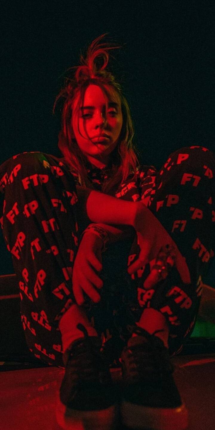Bathed in a dramatic crimson glow, Billie Eilish offers a sullen gaze, her messy top-knot and 'FTP' patterned attire visible in this atmospheric 4K wallpaper. This moody celebrity wallpaper is a must-have for iPhone users seeking an edgy aesthetic. | artist Bathed in a dramatic crimson glow, Billie Eilish offers a sullen gaze, her messy top-knot and 'FTP' patterned attire visible in this atmospheric 4K wallpaper. This moody celebrity wallpaper is a must-have for iPhone users seeking an edgy aesthetic.