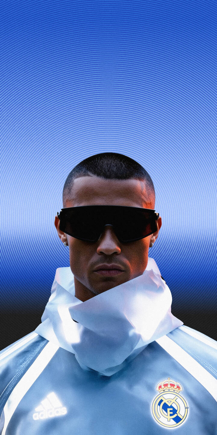 Sleek futuristic sunglasses obscure Cristiano Ronaldo's intense gaze as he stands against a vibrant blue concentric circle background, sporting his Real Madrid adidas gear in this stunning 4K wallpaper. This dynamic wallpaper is a perfect fit for any iPhone, celebrating the iconic footballer's stylish presence. | football blue sunglasses iphone real madrid wallpaper cr7 futuristic cristiano ronaldo mobile 4k wallpaper hd wallpaper Sleek futuristic sunglasses obscure Cristiano Ronaldo's intense gaze as he stands against a vibrant blue concentric circle background, sporting his Real Madrid adidas gear in this stunning 4K wallpaper. This dynamic wallpaper is a perfect fit for any iPhone, celebrating the iconic footballer's stylish presence.