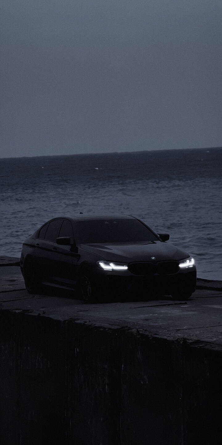 The BMW's piercing white headlights illuminate the twilight dockside, creating a dramatic contrast against the sleek black car and the brooding ocean in this striking 4K wallpaper for iPhone. This moody scene makes for an evocative lock screen wallpaper. | car dark iphone bmw ocean wallpaper mobile luxury car moody 4k wallpaper hd wallpaper automotive The BMW's piercing white headlights illuminate the twilight dockside, creating a dramatic contrast against the sleek black car and the brooding ocean in this striking 4K wallpaper for iPhone. This moody scene makes for an evocative lock screen wallpaper.