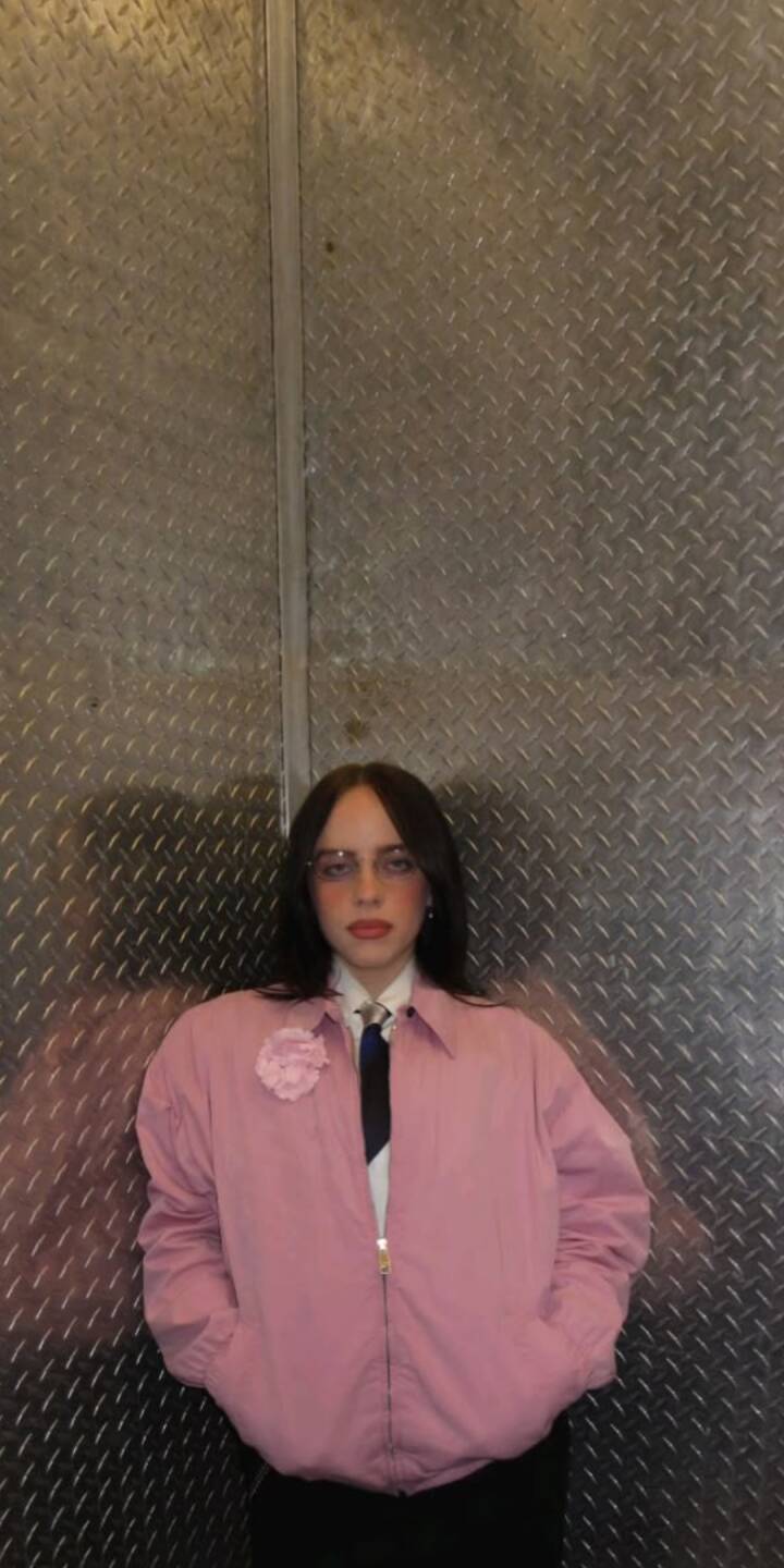 Against a rugged diamond plate metal wall, a person with dark hair, round glasses, and a pink jacket with a coordinating fabric flower brooch holds a composed gaze in this striking 4K wallpaper. This stylish wallpaper for iPhone highlights subtle fashion against an industrial backdrop. | artist Against a rugged diamond plate metal wall, a person with dark hair, round glasses, and a pink jacket with a coordinating fabric flower brooch holds a composed gaze in this striking 4K wallpaper. This stylish wallpaper for iPhone highlights subtle fashion against an industrial backdrop.