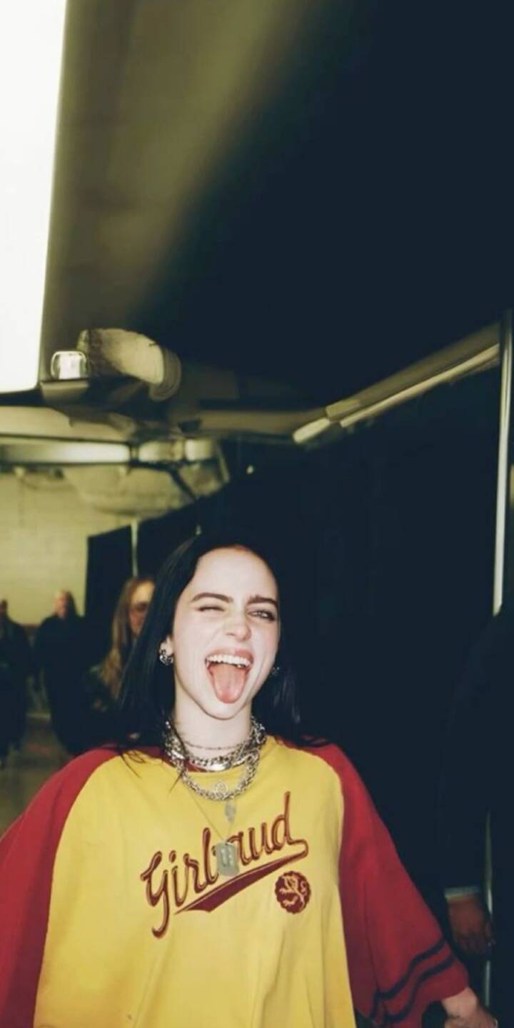 A playful wink and tongue out expression from Billie Eilish captures her edgy personality in this vibrant 4K wallpaper. Featuring her distinctive layered necklaces and a bold yellow and red shirt, this wallpaper is a must-have for iPhone users. | artist A playful wink and tongue out expression from Billie Eilish captures her edgy personality in this vibrant 4K wallpaper. Featuring her distinctive layered necklaces and a bold yellow and red shirt, this wallpaper is a must-have for iPhone users.