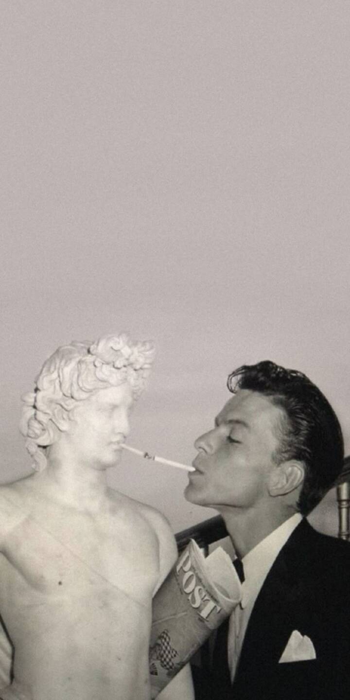 In this striking 4K wallpaper, Frank Sinatra is playfully seen lighting a cigarette from the mouth of a classical marble statue, with a rolled 'POST' newspaper in hand. This unique, vintage-style wallpaper makes an artistic statement on any iPhone screen. | artist In this striking 4K wallpaper, Frank Sinatra is playfully seen lighting a cigarette from the mouth of a classical marble statue, with a rolled 'POST' newspaper in hand. This unique, vintage-style wallpaper makes an artistic statement on any iPhone screen.