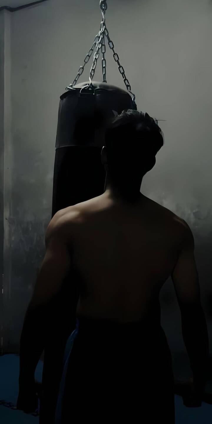 A powerful silhouette of a muscular individual, bathed in dim light, stands ready to engage a heavy punching bag in this intense 4K wallpaper. This atmospheric gym wallpaper for iPhone captures the gritty determination of a fighter in training. | sort A powerful silhouette of a muscular individual, bathed in dim light, stands ready to engage a heavy punching bag in this intense 4K wallpaper. This atmospheric gym wallpaper for iPhone captures the gritty determination of a fighter in training.