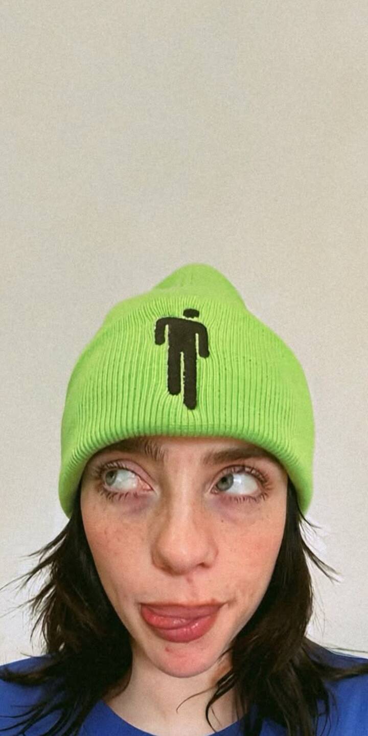 Billie Eilishโs signature playful expression shines through in this vibrant 4K wallpaper, with her eyes playfully rolled up and tongue slightly out. Her striking bright green beanie, featuring the iconic 'Blohsh' figure, makes this an unmissable aesthetic wallpaper for iPhone users. | artist Billie Eilishโs signature playful expression shines through in this vibrant 4K wallpaper, with her eyes playfully rolled up and tongue slightly out. Her striking bright green beanie, featuring the iconic 'Blohsh' figure, makes this an unmissable aesthetic wallpaper for iPhone users.
