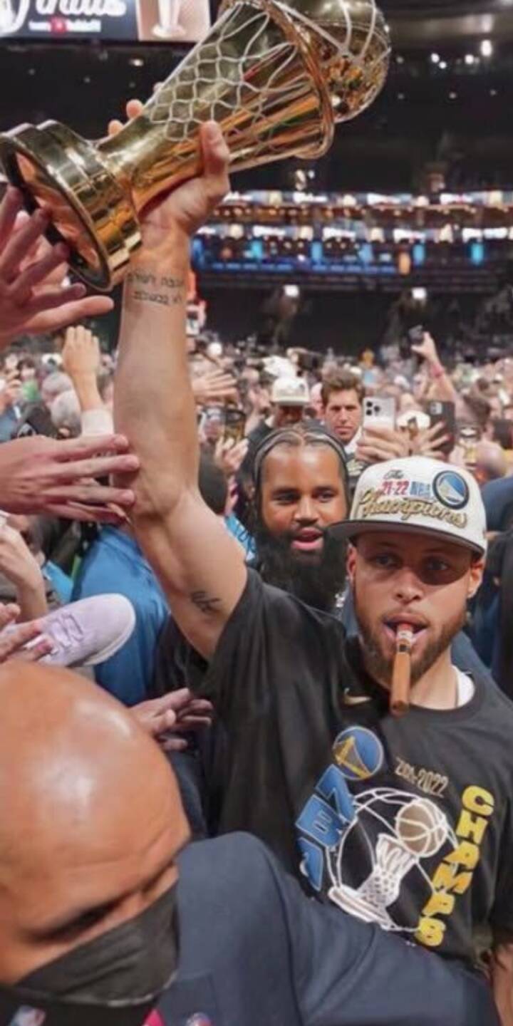 Steph Curry poses with a lit cigar in his mouth, wearing his 2022 Champions hat and shirt, while a teammate holds the golden trophy high in this vibrant 4K wallpaper. This spirited celebration wallpaper is a must-have for any iPhone, capturing the thrill of victory. | artist Steph Curry poses with a lit cigar in his mouth, wearing his 2022 Champions hat and shirt, while a teammate holds the golden trophy high in this vibrant 4K wallpaper. This spirited celebration wallpaper is a must-have for any iPhone, capturing the thrill of victory.