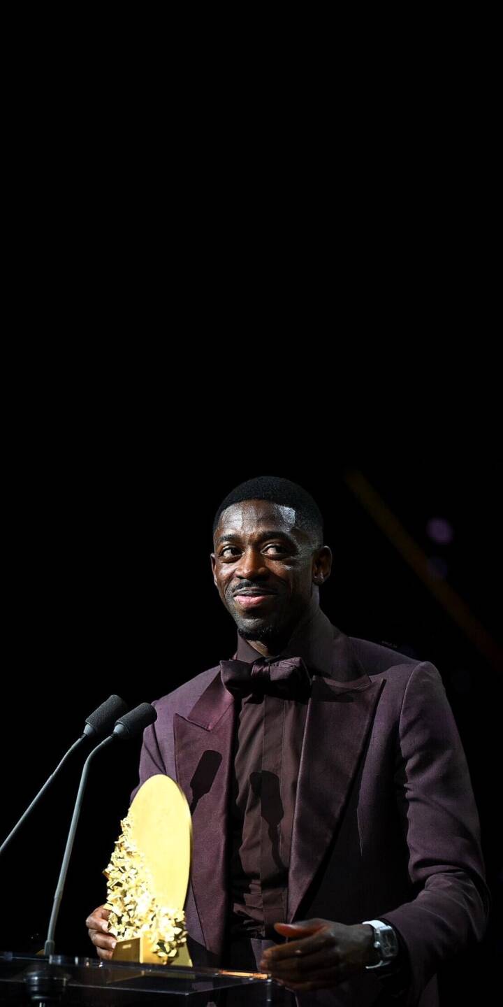 Ousmane Dembélé grins warmly while accepting a uniquely textured golden trophy, dressed sharply in a rich burgundy suit and bow tie, making this a celebratory 4K wallpaper perfect for your iPhone. This exclusive wallpaper captures the footballer in a moment of triumph at the podium. | football trophy athlete iphone wallpaper mobile 4k wallpaper hd wallpaper dembele ousmane dembélé award burgundy Ousmane Dembélé grins warmly while accepting a uniquely textured golden trophy, dressed sharply in a rich burgundy suit and bow tie, making this a celebratory 4K wallpaper perfect for your iPhone. This exclusive wallpaper captures the footballer in a moment of triumph at the podium.