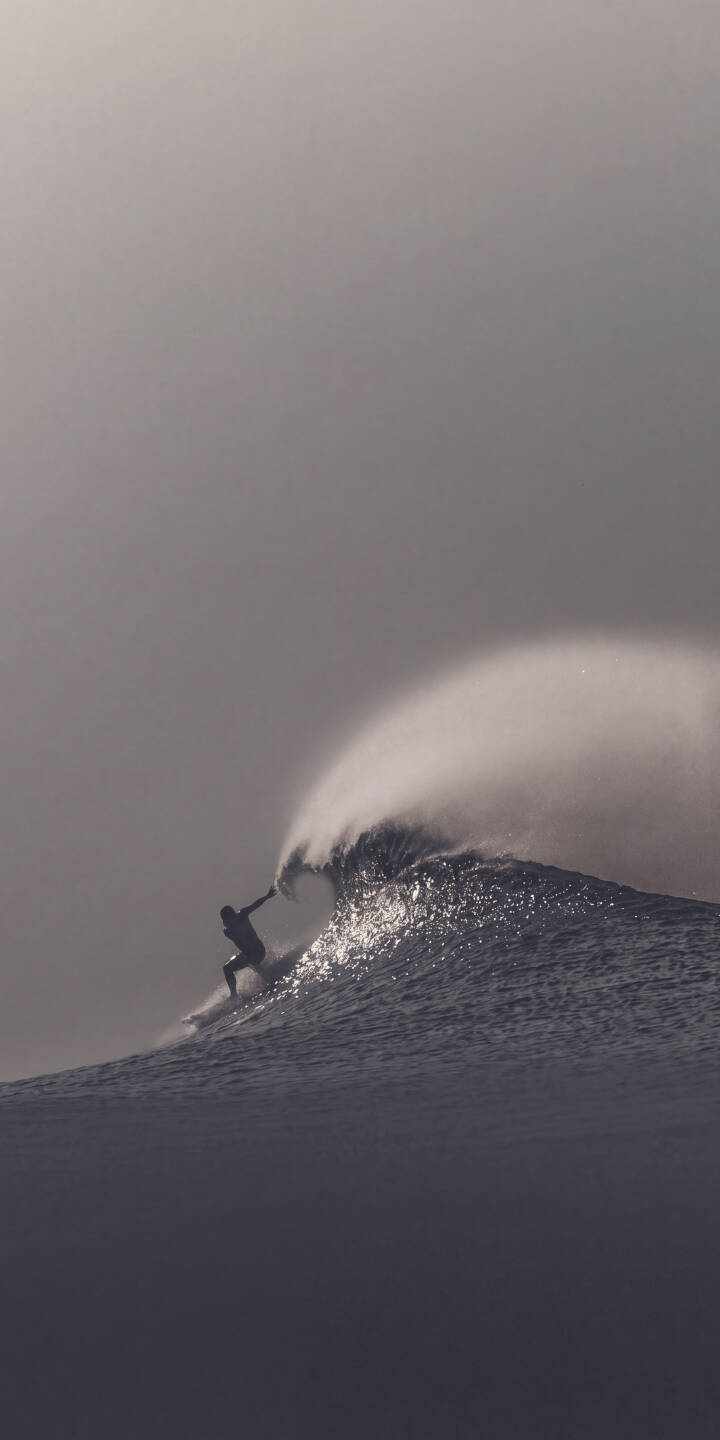 A lone surfer, silhouetted against a muted gray sky, expertly rides a massive, breaking ocean wave in this stunning 4K wallpaper. The dramatic spray from the wave's crest adds to the intense atmosphere of this dynamic wallpaper, perfect for iPhone users. | wave surfer iphone ocean dynamic wallpaper surfing grayscale action mobile 4k wallpaper hd wallpaper A lone surfer, silhouetted against a muted gray sky, expertly rides a massive, breaking ocean wave in this stunning 4K wallpaper. The dramatic spray from the wave's crest adds to the intense atmosphere of this dynamic wallpaper, perfect for iPhone users.