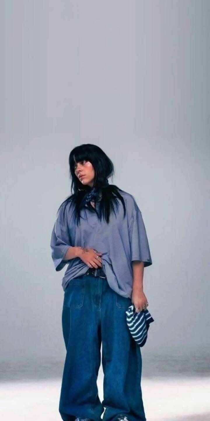 Billie Eilish strikes a relaxed pose in her signature oversized pale blue shirt and baggy blue jeans against a clean studio background in this vibrant 4K wallpaper — the perfect casual yet stylish wallpaper for iPhone users who love her iconic aesthetic. | artist Billie Eilish strikes a relaxed pose in her signature oversized pale blue shirt and baggy blue jeans against a clean studio background in this vibrant 4K wallpaper — the perfect casual yet stylish wallpaper for iPhone users who love her iconic aesthetic.